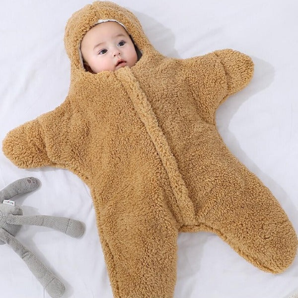 a cute baby dressed up into a honey-brown Baby Star Costume | Winter One PieceBaby Star Costume | Winter One Piece is lying on a soft cosy bed looking like a starfish