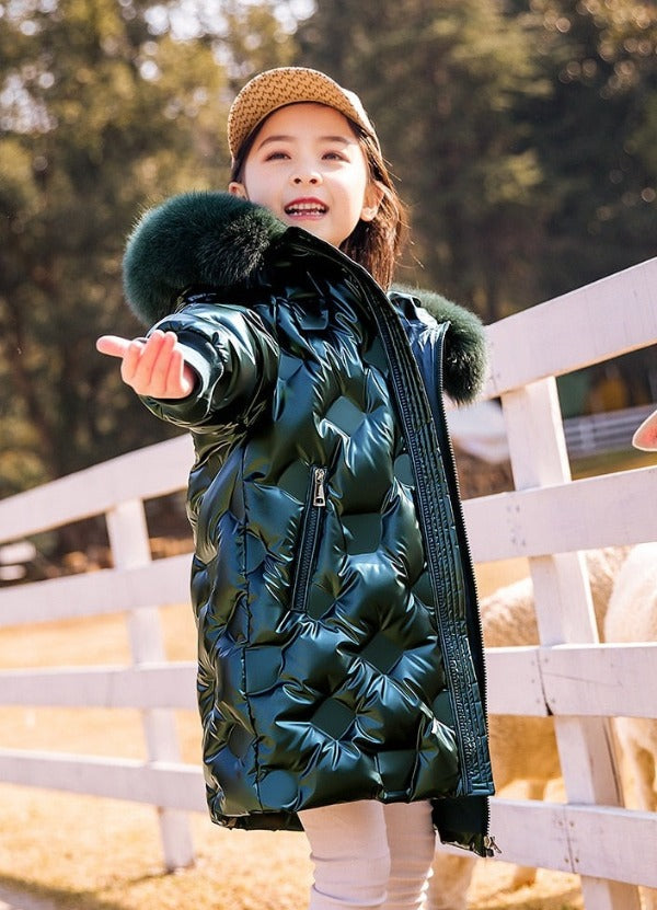 a smiling 8 year old girl  wearing a Long Quilted Coat is stretching her arm as if she was checking whether it is raining or not